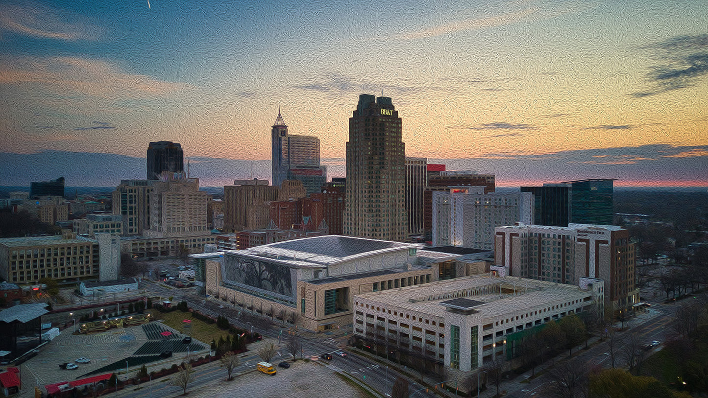 Aerial view of downtown Raleigh, North Carolina, with city skyline illuminated by sunrise.